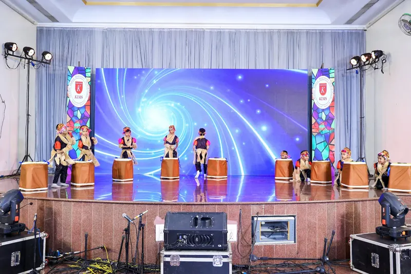 Drummers perform on a stage lit in blue