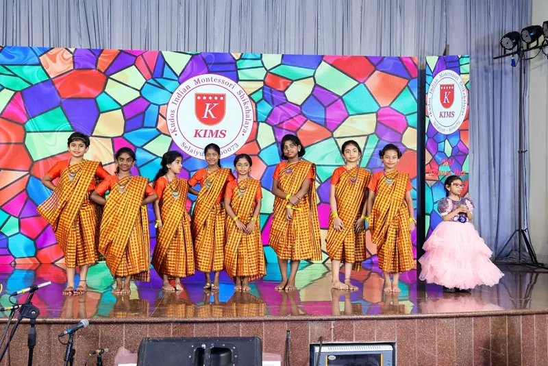 Girls in orange sarees perform a traditional dance