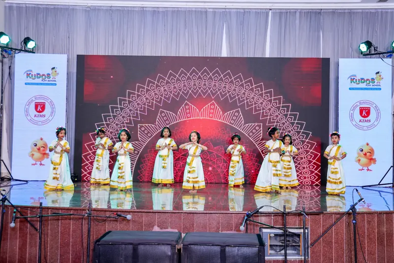 A dance in white and gold in front of a red mandala backdrop
