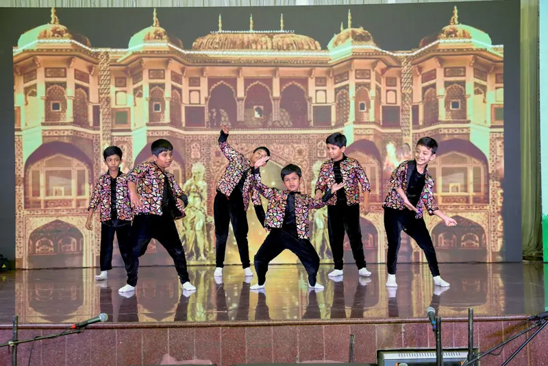 Boys in sequinned jackets dance in front of a palace backdrop