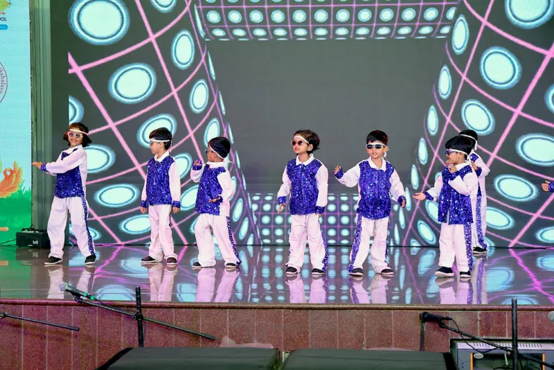 Children in blue waistcoats and sunglasses dance under disco lights