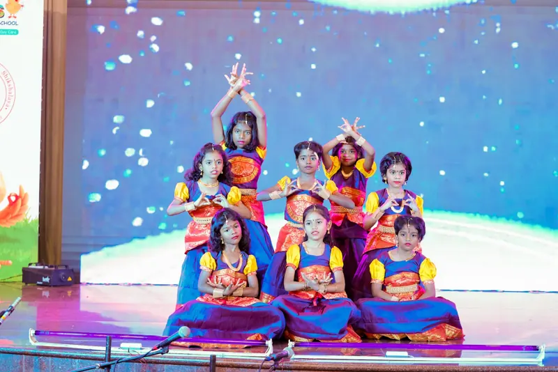 Girls in classical dress sit in a dance formation
