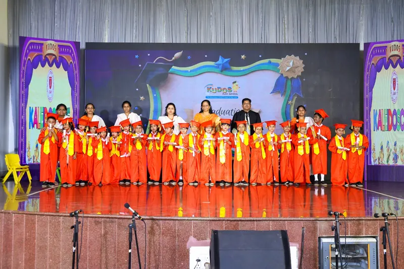 Children in orange costumes fill the stage
