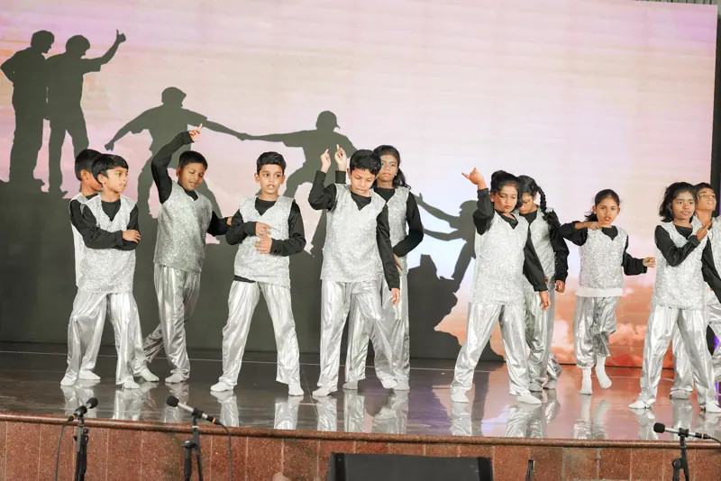 Dancers in silver jackets in front of a city-skyline backdrop