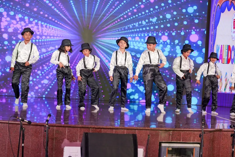 Children in hats and braces dance under disco lights