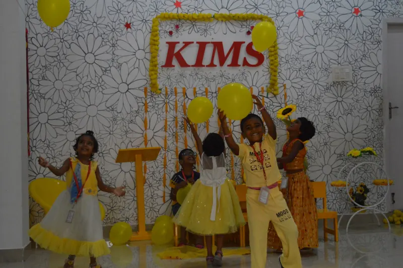 Children play with yellow balloons under the KIMS sign