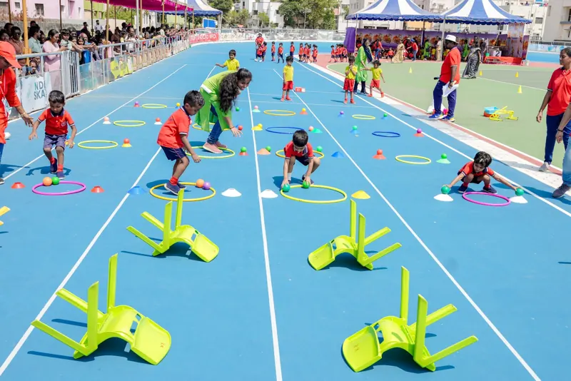 Children race through an obstacle course of chairs and hoops